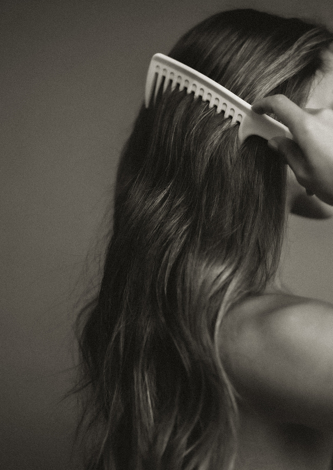Person combing their hair extensions with a white comb against a plain background